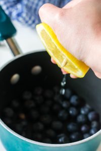 squeezing a lemon into blueberries cooking in a pot