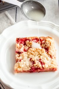 Drizzling the frosting mixture over The best white peach strawberry bars