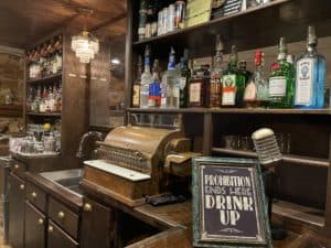 Picture of a prohibition era speakeasy with cash register and alcohol bottles lining the wall