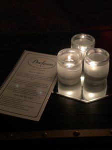 Picture of a menu next to candles in a dark speakeasy