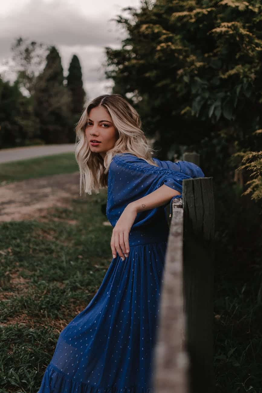 woman in blue dress leaning on wooden fence