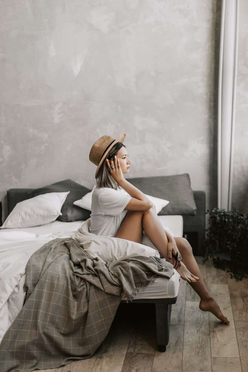 home comfort; woman in white dress shirt sitting on bed