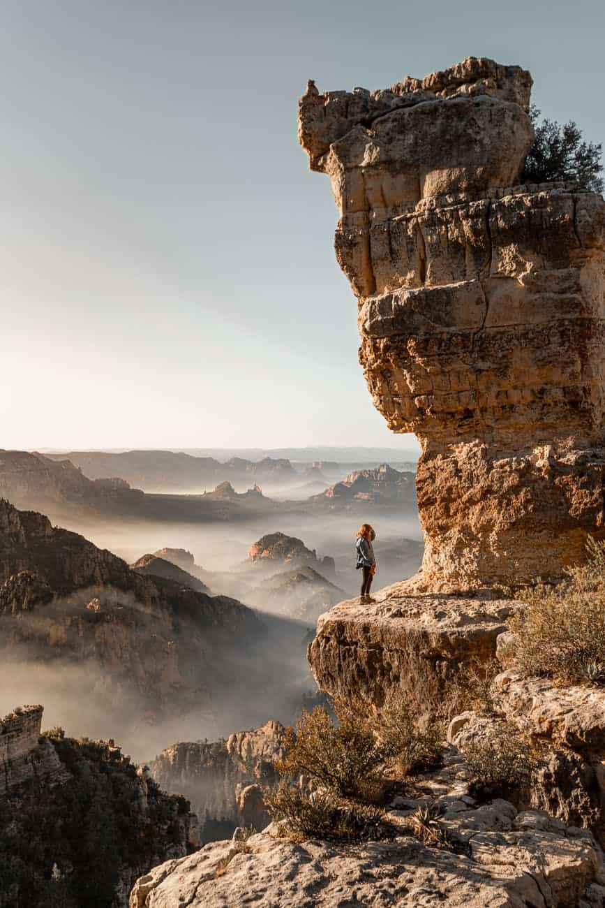 unrecognizable tourist standing under rough cliff in mountains during vacation