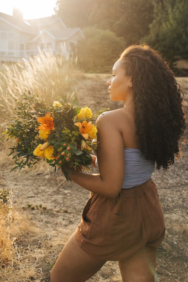 woman in gray off shoulder top and brown shorts holding yellow flower