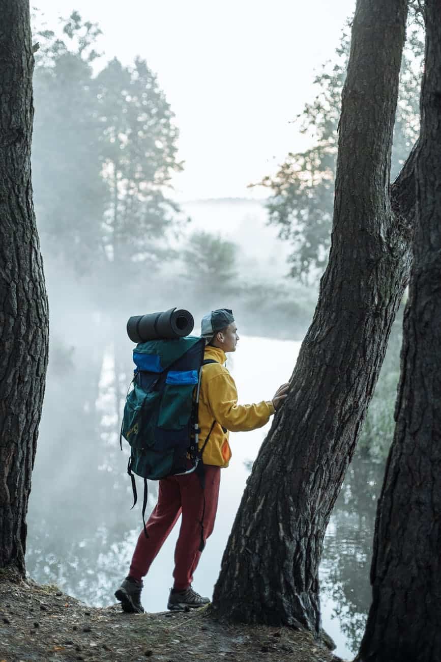 a man carrying his backpack standing next to a tree