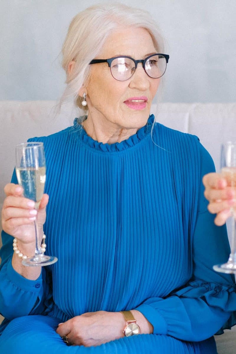 elderly women in eyeglasses with glasses of champagne talking