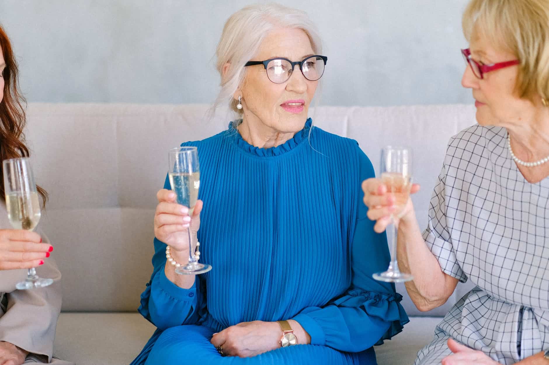 elderly women in eyeglasses with glasses of champagne talking