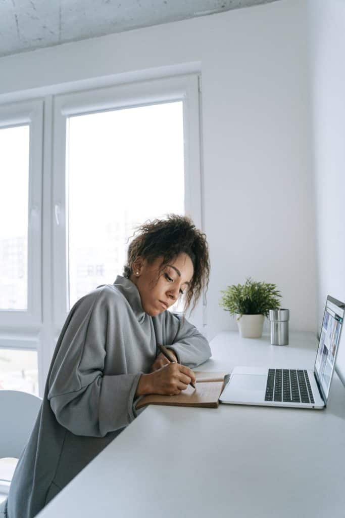 a woman writing on her notebook in front of her laptop; maintenance of business