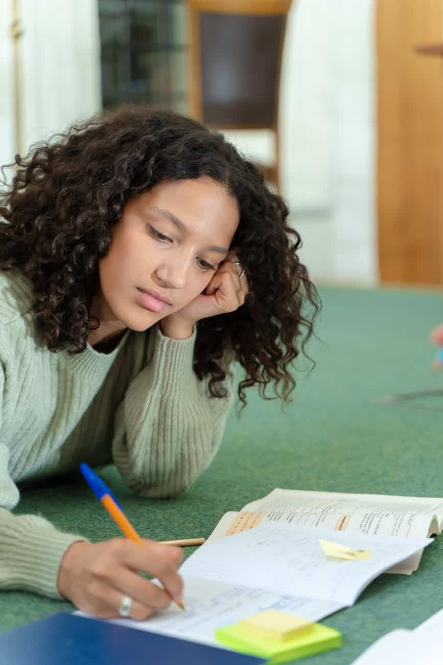 bored student writing on a textbook while on the floor