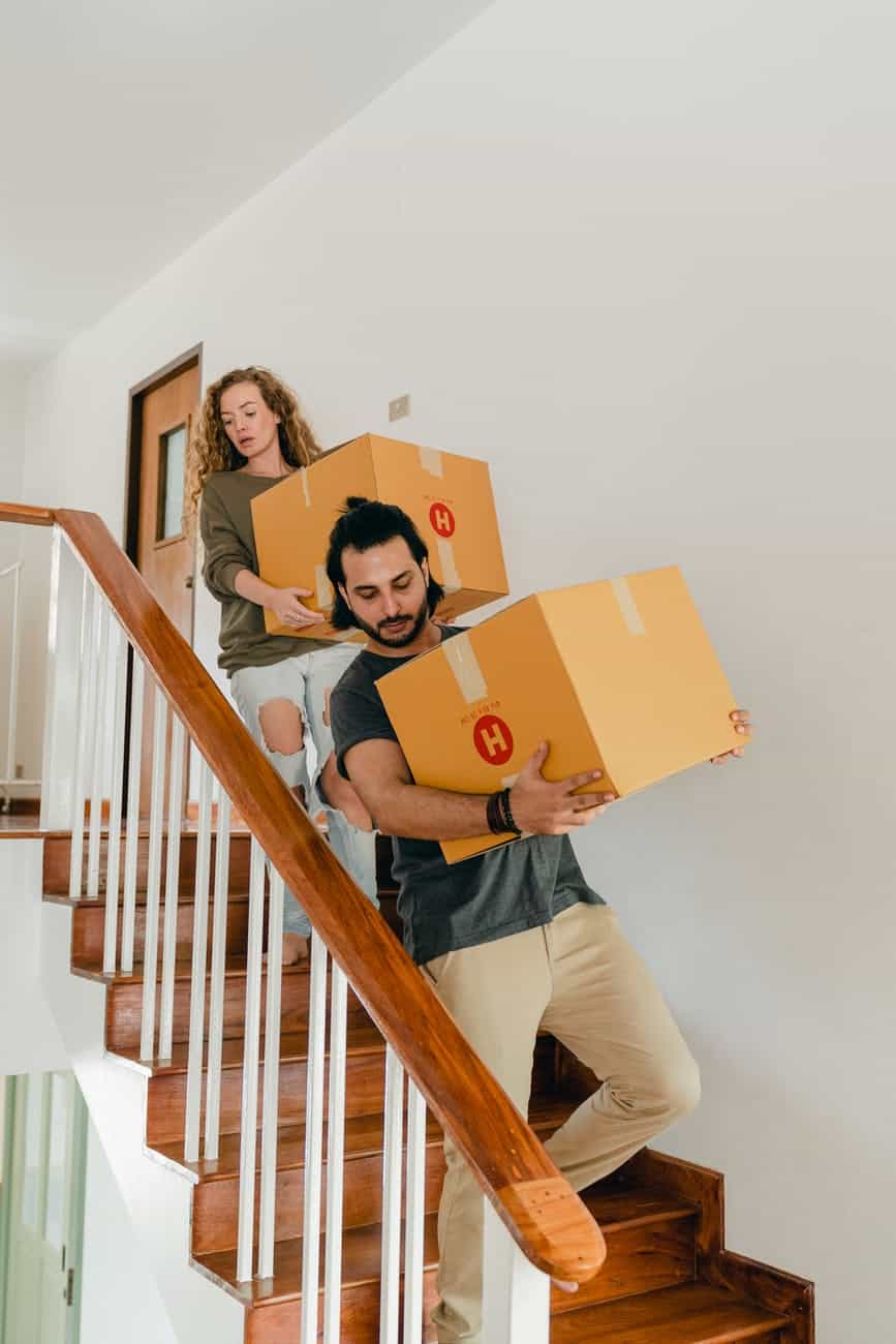 focused couple carrying boxes on stairs