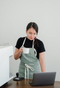 young barista watching video on laptop while enjoying coffee break