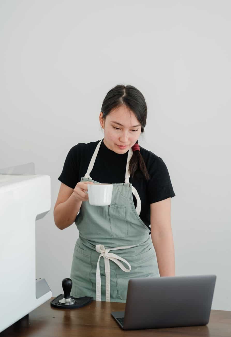 young barista watching video on laptop while enjoying coffee break