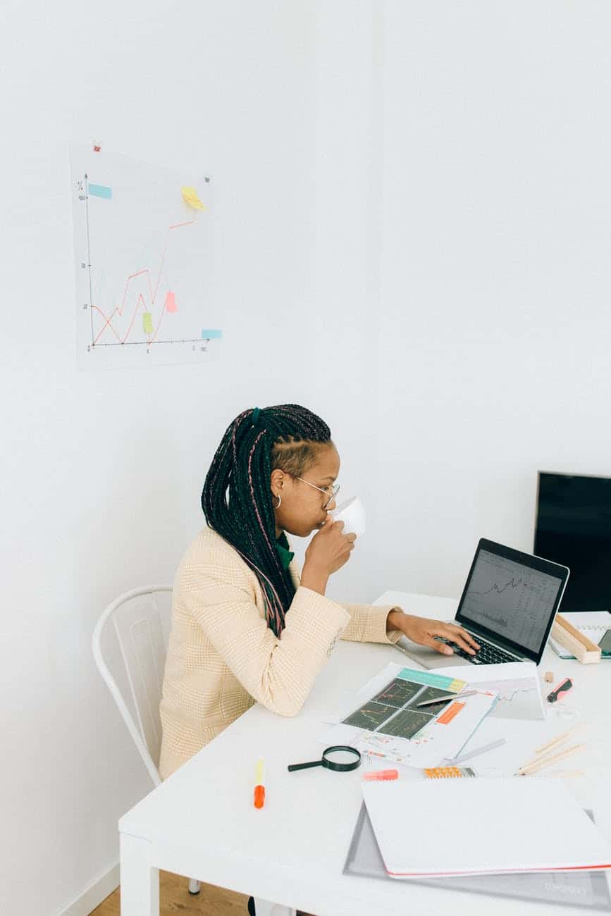 woman drinking beverage while working on laptop