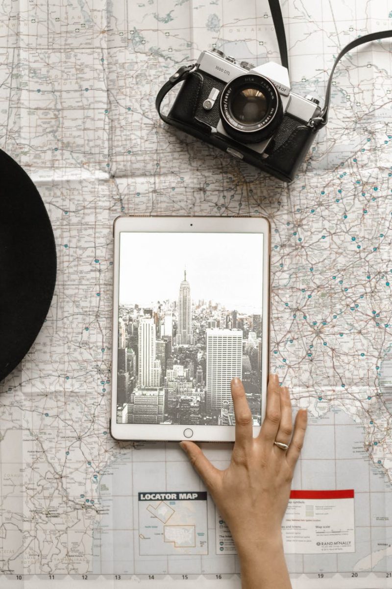 flat lay photography of person touching silver ipad on world map chart beside black hat