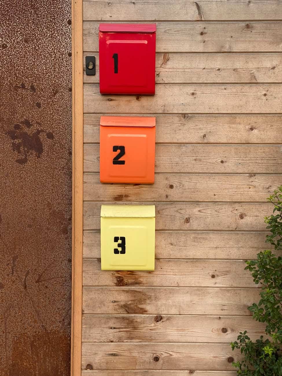 colorful mailboxes on wooden wall near door and plant
