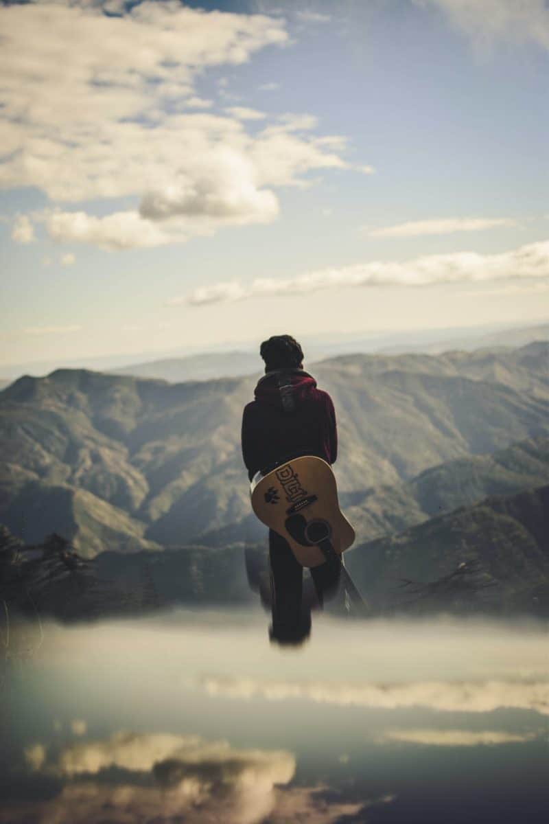 man carrying guitar while standing starring at the hills