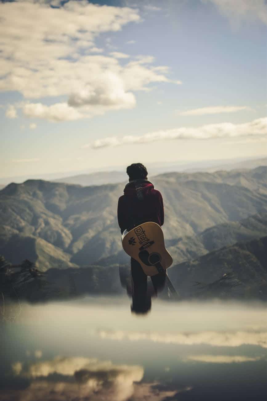 man carrying guitar while standing starring at the hills