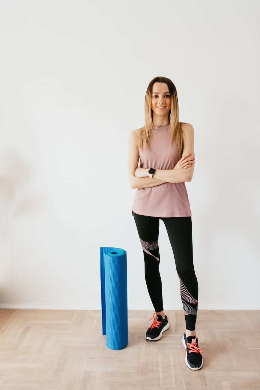 slim sportswoman with folded yoga mat at home