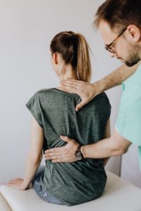 crop osteopath examining back of anonymous woman in doctor office