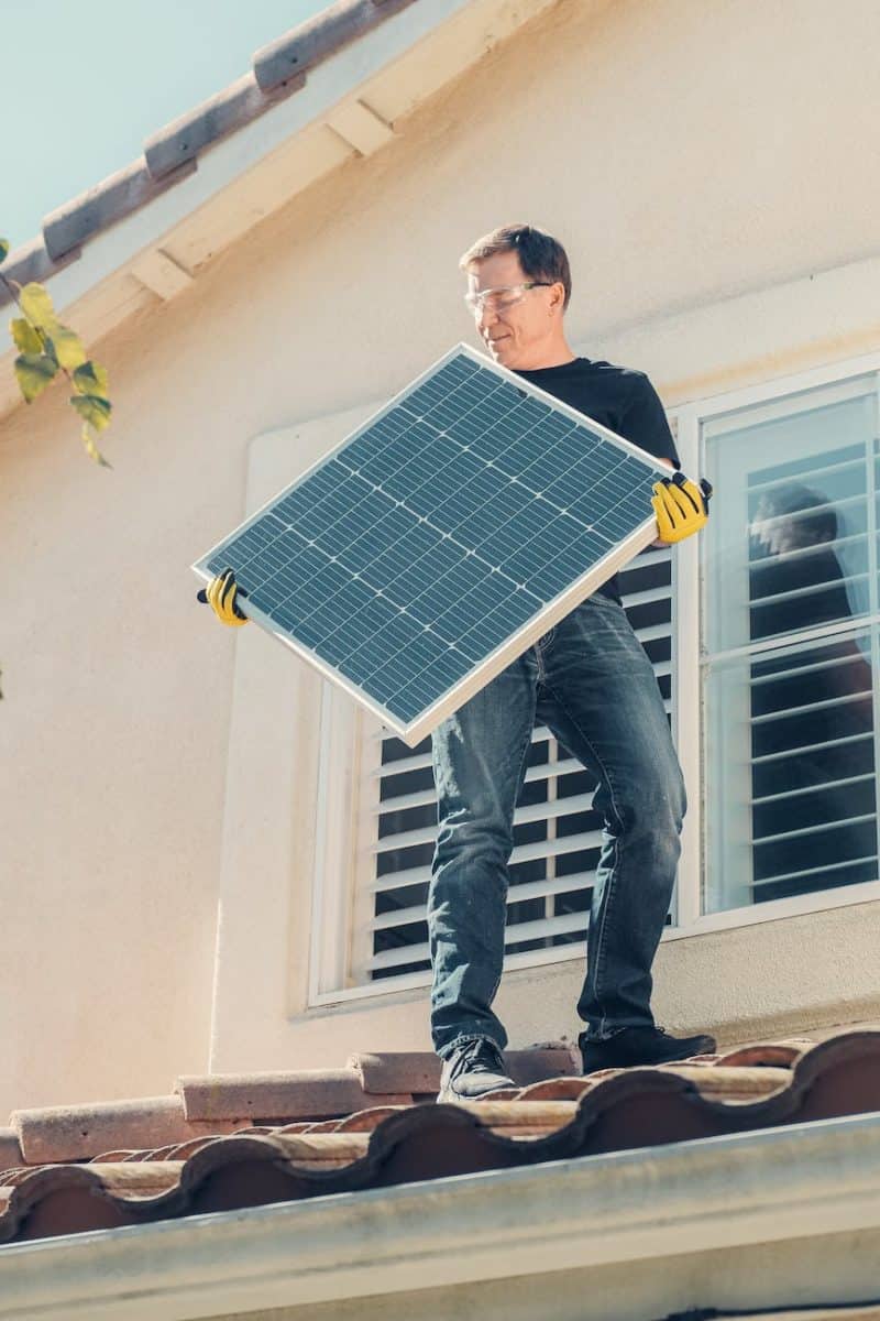 a man in black shirt standing on the roof while holding a solar panel