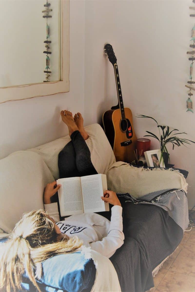 woman reading book while lying on sofa