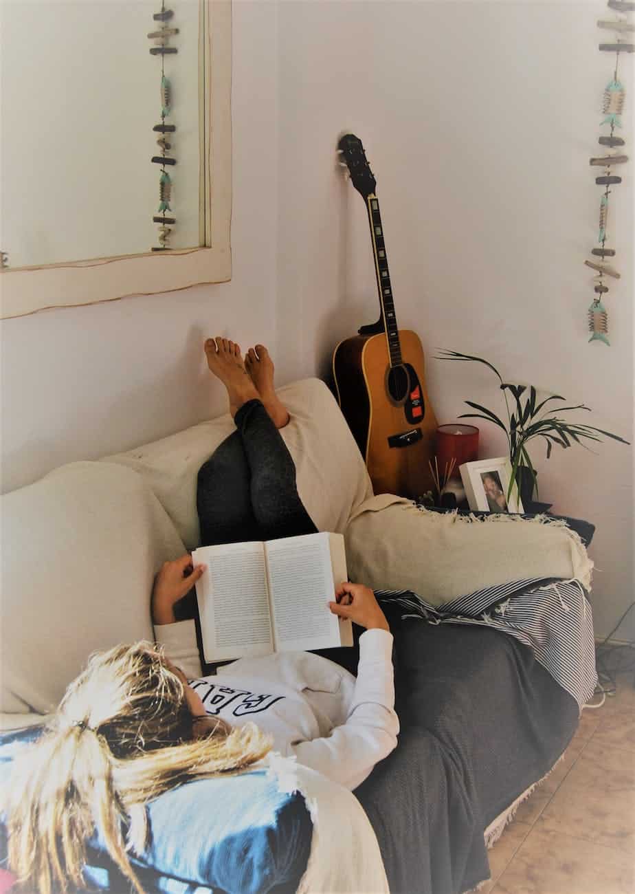 woman reading book while lying on sofa