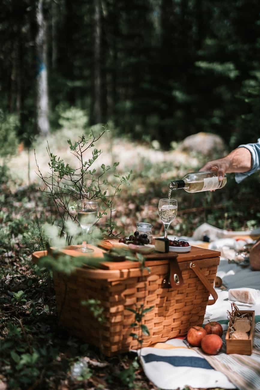 person pouring wine on a glass above a wicker basket