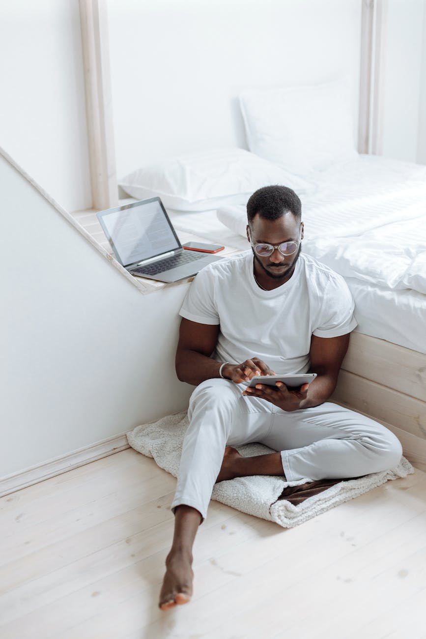 a man sitting on the white blanket on the floor while using his tablet