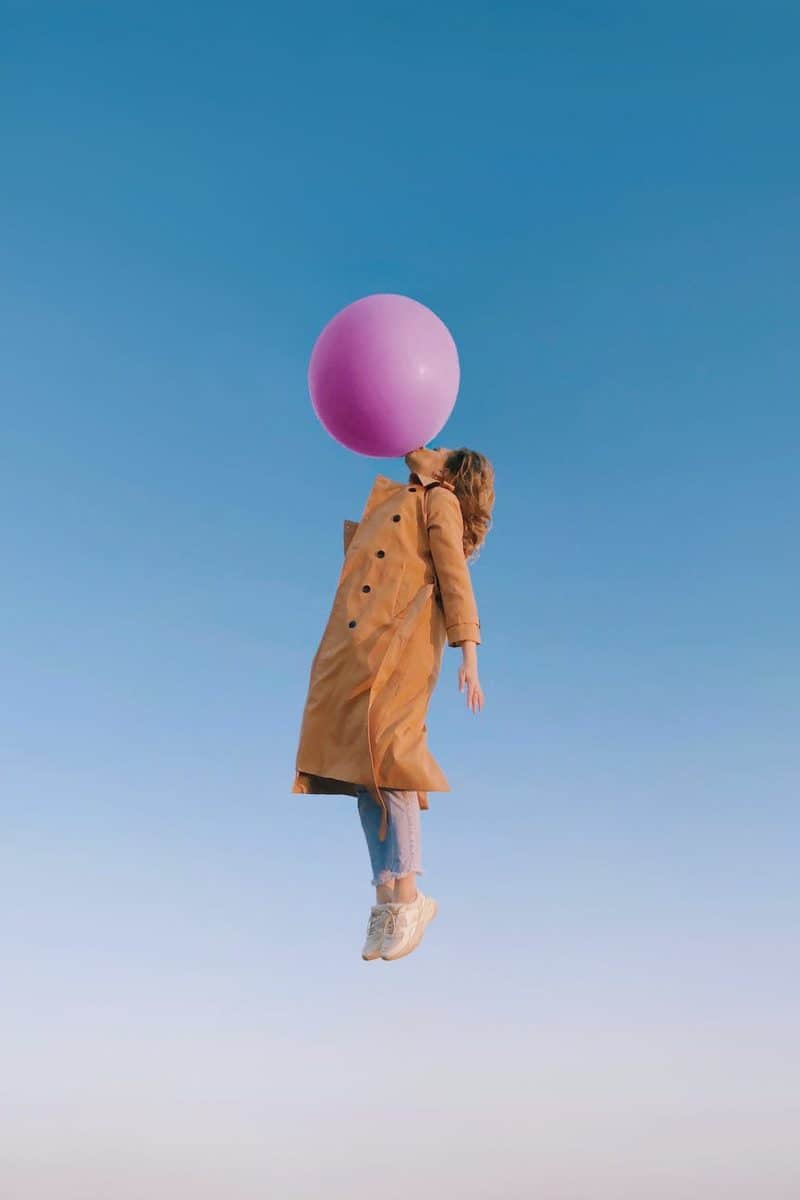 young female blowing huge balloon in sky