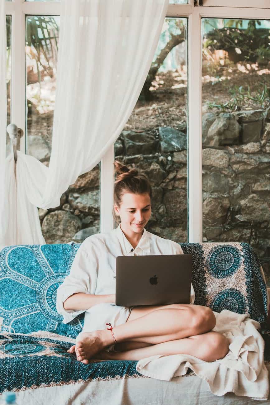 smiling woman using macbook while sitting on sofa