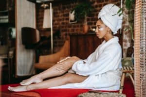 woman in bathrobe applying cream on leg