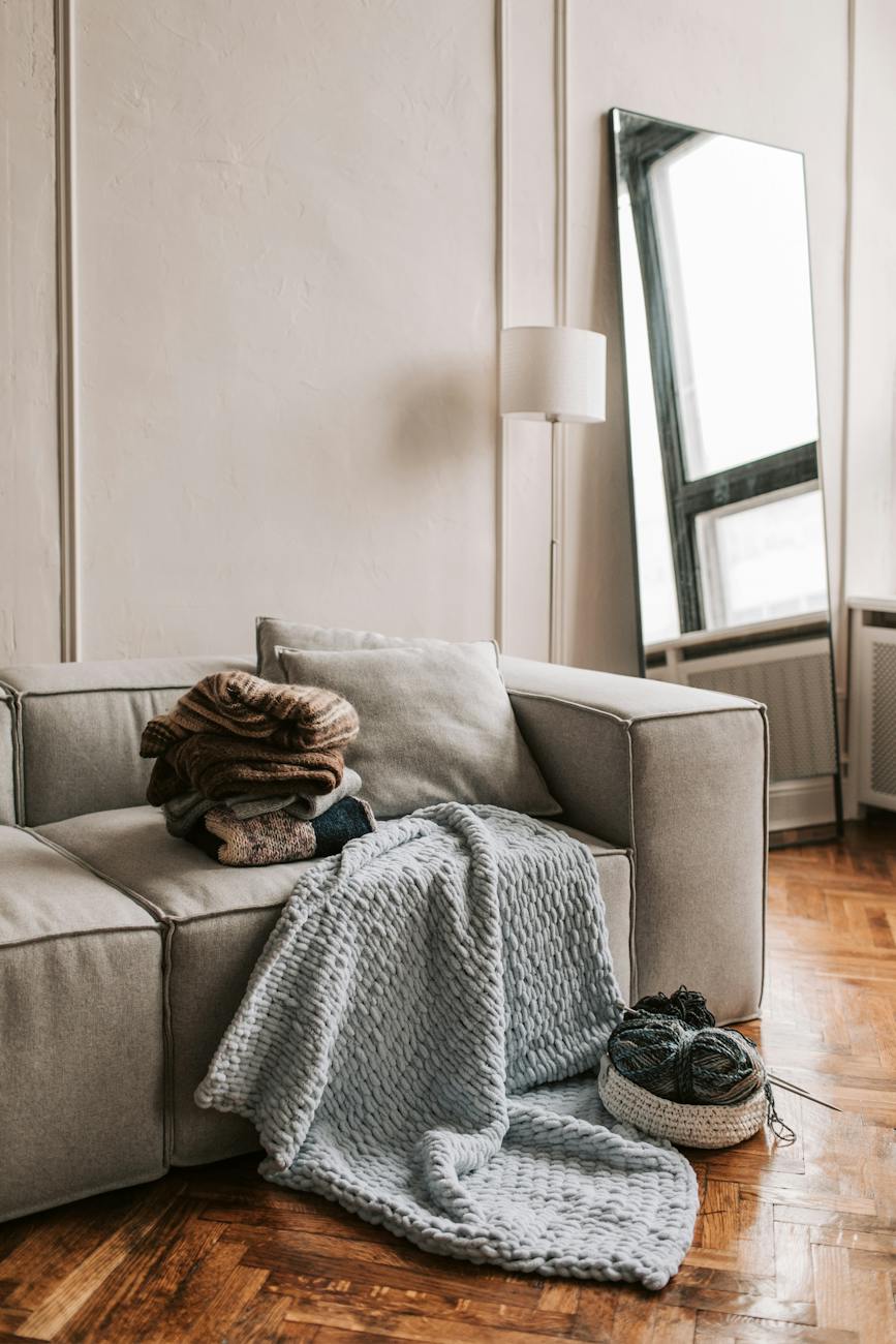 a pile of sweaters and a bowl with yarn on a sofa in a room