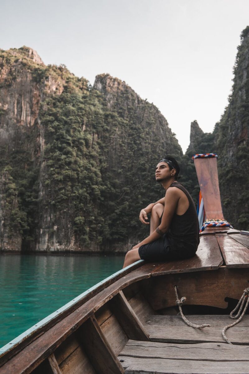 man in black tank top sitting on brown boat on body of water