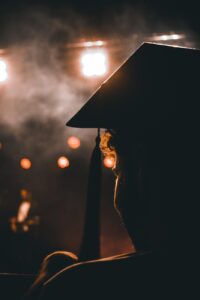 silhouette of a person in a mortarboard looking at an illuminated stage