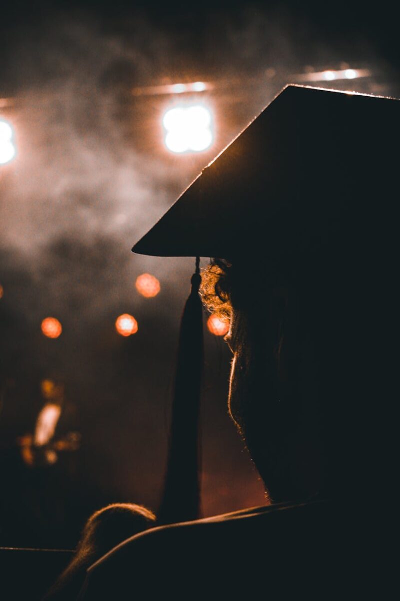 silhouette of a person in a mortarboard looking at an illuminated stage