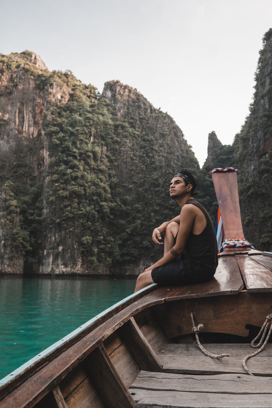 man in black tank top sitting on brown boat on body of water