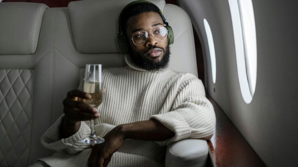 Man sitting in a luxury airplane seat with headphones, enjoying a glass of champagne, looking relaxed.