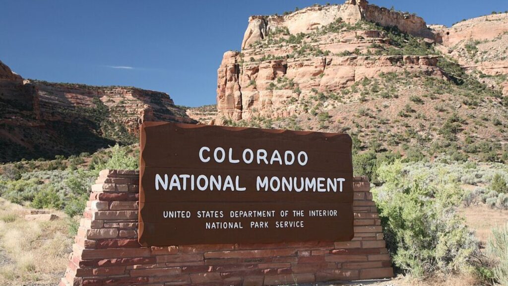 Entrance sign at Colorado National Monument with red rock cliffs in the background.