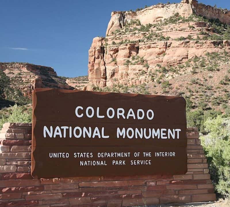 Entrance sign at Colorado National Monument with red rock cliffs in the background.