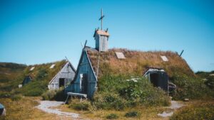 Reconstructed Viking turf houses with grass-covered roofs and wooden walls, set in a remote field under a bright blue sky.