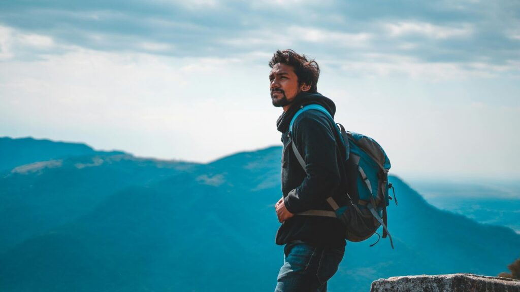 Solo traveler with backpack looking out over mountain landscape under cloudy sky.