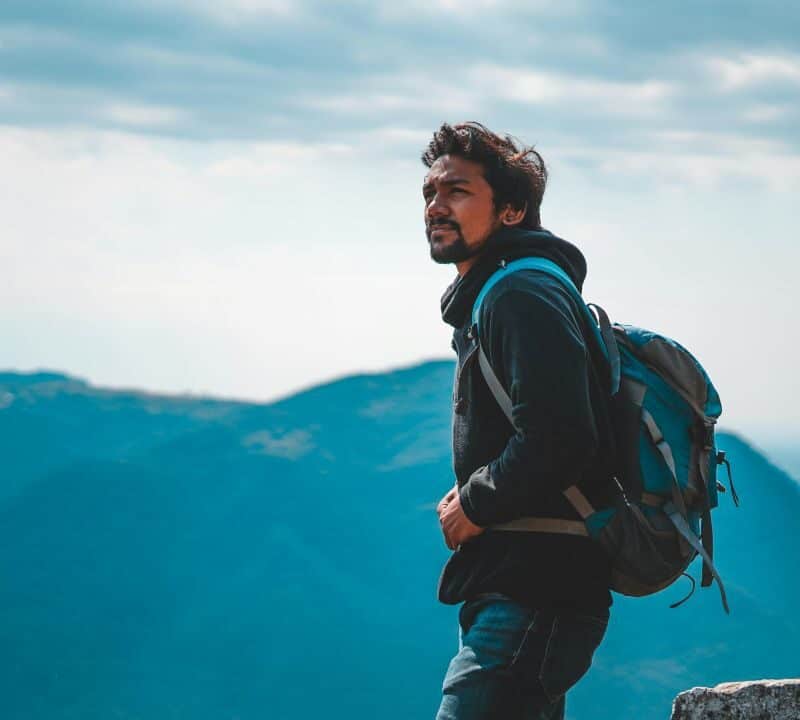 Solo traveler with backpack looking out over mountain landscape under cloudy sky.