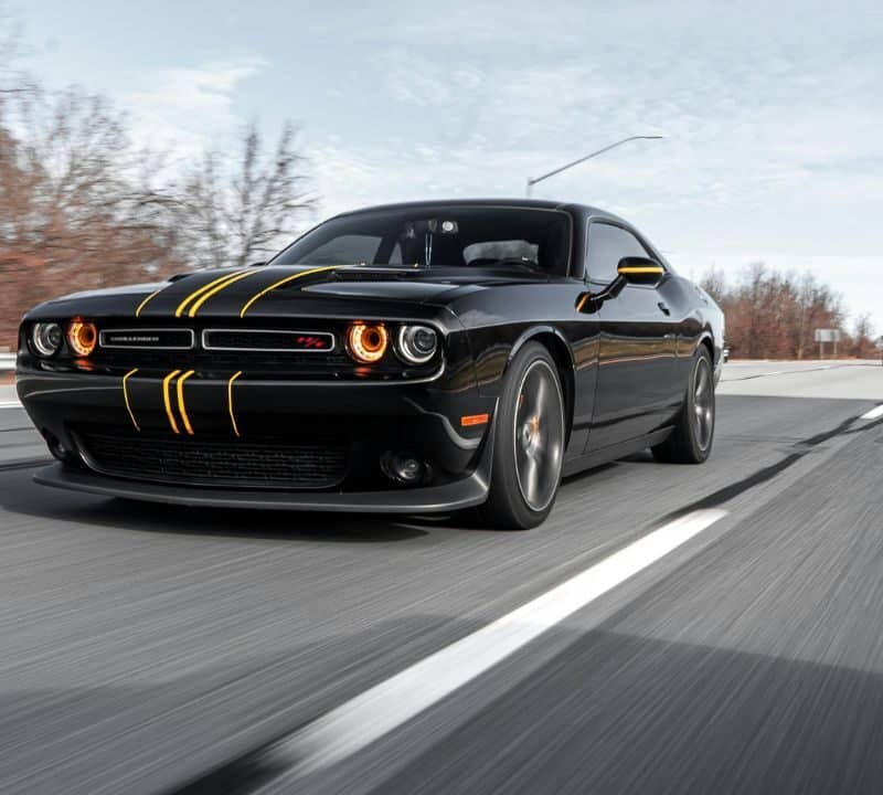 Black sports car with yellow racing stripes driving fast on a highway, representing alert and smart travel on the road.