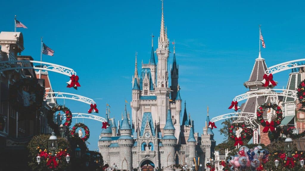 Cinderella Castle at Disney World decorated for the holidays with wreaths, ribbons, and American flags on a sunny day.