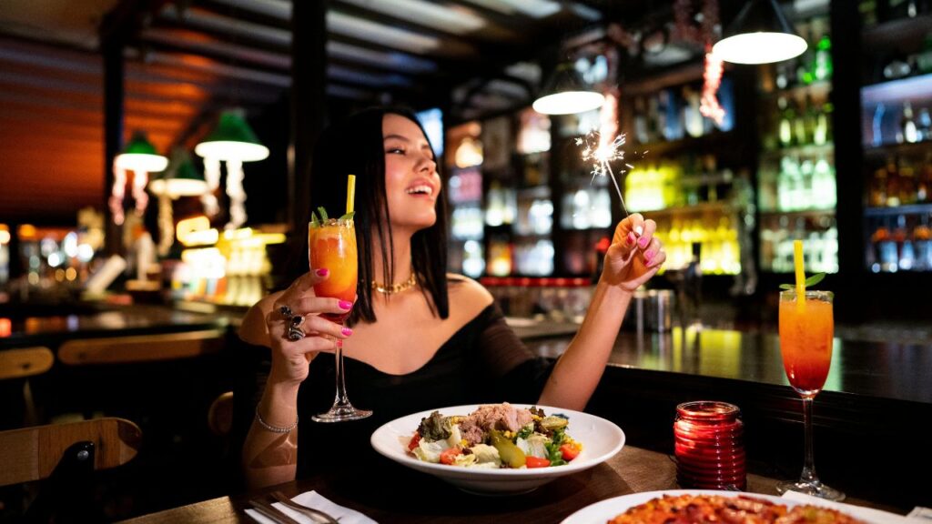 Woman enjoying a romantic dinner with a sparkler and cocktail in a dimly lit restaurant, evoking a date night vibe.