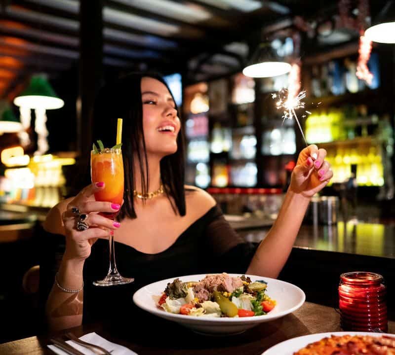 Woman enjoying a romantic dinner with a sparkler and cocktail in a dimly lit restaurant, evoking a date night vibe.