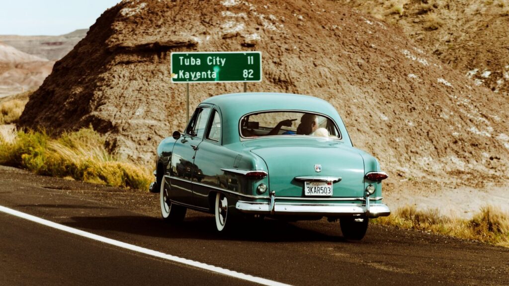 Vintage teal car cruises a desert road near Tuba City, evoking classic ’70s road trip nostalgia.