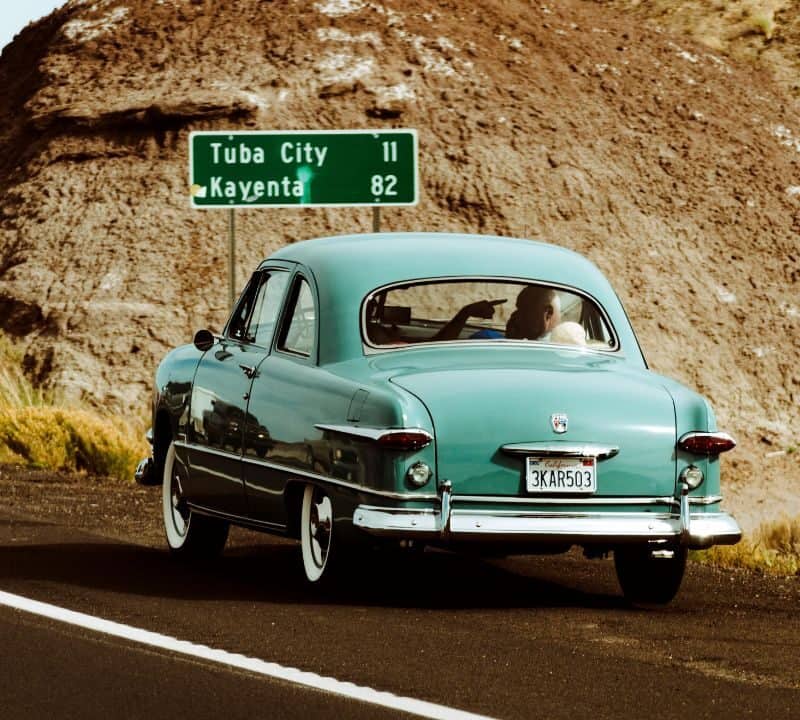 Vintage teal car cruises a desert road near Tuba City, evoking classic ’70s road trip nostalgia.