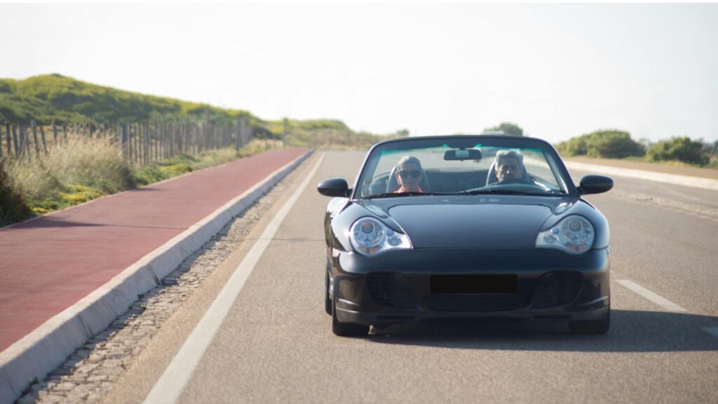 Two people driving a black convertible down an empty scenic road, enjoying a sunny road trip adventure.