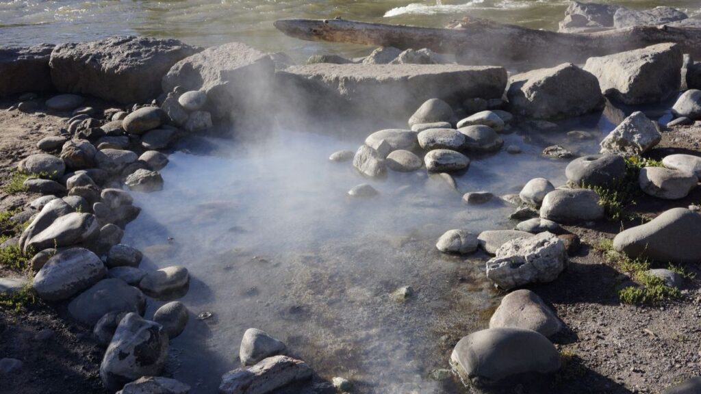 Steam rising from a natural rock-lined hot spring along a riverbank in Idaho, perfect for a relaxing weekend soak.